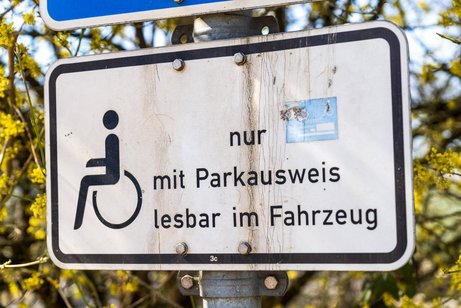 Ein Verkehrsschild an einem Behindertenparkplatz mit einem Rollstuhl-Symbol und dem Text "nur mit Parkausweis lesbar in Fahrzeug".