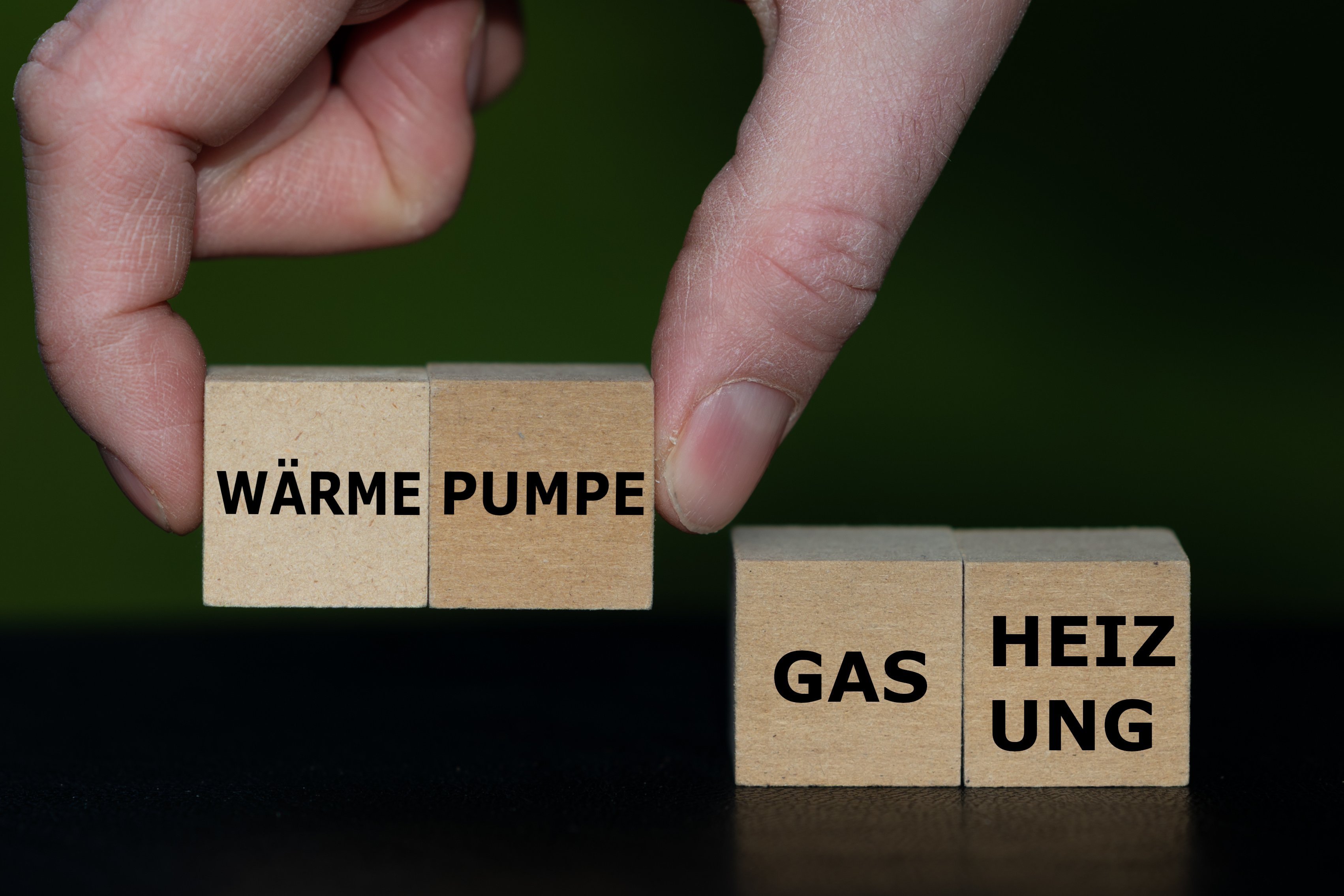 Eine Hand setzt Holzw&uuml;rfel mit W&ouml;rtern zusammen, sie bilden die Worte "W&auml;rme-Pumpe" und "Gas-Heizung"