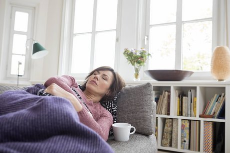 Erschöpfung nach Covid-Erkrankung Eine Frau liegt erschöpft auf einer Couch unter einer Decke.