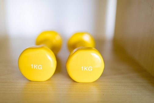 Zwei gelbe Ein-Kilo-Hanteln liegen auf einem Holzboden