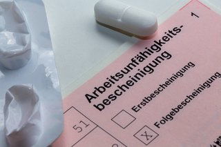 Eine Arbeitsunfähigkeitsbescheinigung, auf der "Folgebescheinigung" angekreuzt ist, und Tabletten