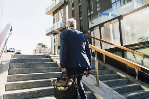 Älterer Arbeitnehmer Ein älterer Mann im Business-Anzug und mit Aktentasche läuft eine Treppe hinaus, man sieht ihn von hinten