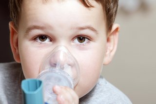 Ein kleiner Junge hält sich einen Inhalator, wie er bei Asthma verwendet wird, über Mund und Nase. 