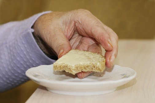 Die Hand einer Frau in einem Altersheim greift nach einem Buttebrot