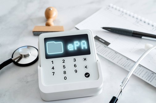 Ein Kartenleseger&auml;t, auf dessen Display "ePA" steht. Au&szlig;erdem liegen auf dem Tisch ein Stethoskop, ein Kalender mit Kugelschreibe und ein Stempel.