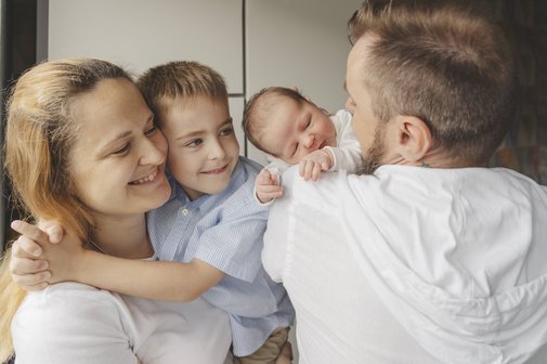 Eine Familie steht eng zusammen, die Mutter hat eine kleinen Jungen auf dem Arm, der Vater ein wenige Wochen altes Baby.