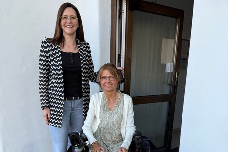 Manuela Ernst, im Rollstuhl, und Franziska Geiß stehen nebeneinander vor einer Tür mit elektrischem Türantrieb.