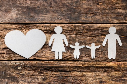 Eine aus Papier ausgeschnittene Familie mit Vater, Mutter und zwei Kindern auf h&ouml;lzernem Untergrund